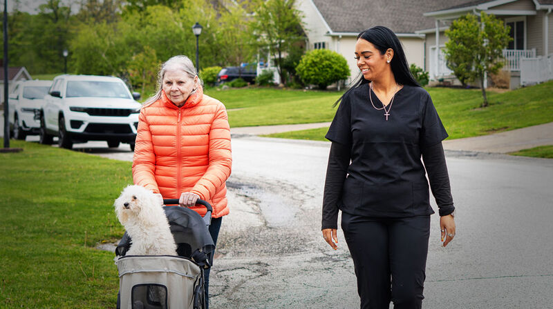 A caregiver and a woman walking her dog down a residential street